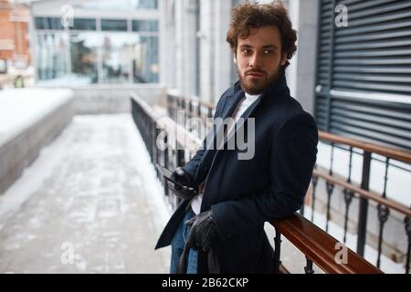 Seltsamer Mann in Handschuhen, der eine Tasche mit Geld hält, Drogen auf der Straße auswählend, gut aussehender bärtiger Mann, der auf einen Kunden wartet, Kunden, Interesse, Hobby Stockfoto