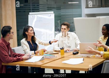 Junge brünette elegante Frau, die ihren Kollegen Dokumente gibt, ein Blatt Papier gibt, um sie zu überprüfen und das Produkt anzubieten. Nahaufnahme Foto. Stockfoto