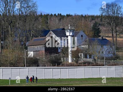 09. März 2020, Thüringen, Mödlareuth: Die Mauer und ein Wachturm stehen mitten im Dorf. Wie Berlin war auch das 50-Einwohner-Dorf an der Grenze zwischen Bayern und Thüringen jahrzehntelang zweigeteilt durch eine Mauer. Mit 100 Metern ist das mehr als drei Meter hohe Gebäude als Teil des deutsch-deutschen Museums im Ort geblieben. Foto: Martin Schutt / dpa-Zentralbild / dpa Stockfoto