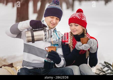 Ein Paar gießt Tee im Becher aus Thermoskannen im Winter Park. Nahaufnahme. Stockfoto