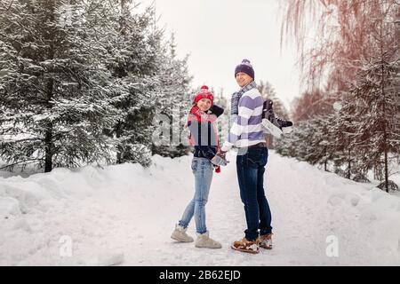 Liebevolles Paar, das an einem Datum in einem Winterpark spazieren geht. Auf der Rückseite eines Kerls hängt ein Paar Schlittschuhe. Stockfoto