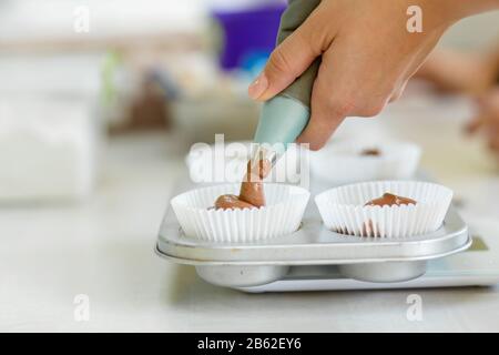 Frau professioneller Konditormeister verteilt Schokoladenteig in Backform. Stockfoto