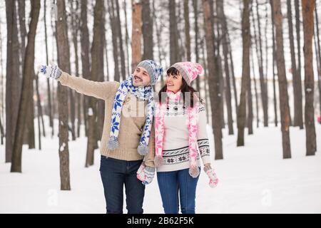 Liebespaar küsst sich im Wald im Winter Pullover. Der Typ zeigt mit der Hand an. Stockfoto