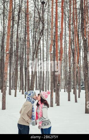 Urlaubs-, Winter-, weihnachts-, Liebes- und Personen-Konzept - glückliches Paar küsst sich im Wald unter Tannen im Schnee. Stockfoto