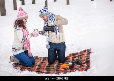 Ein Paar gießt Tee im Becher aus Thermoskannen im Winter Park. Stockfoto