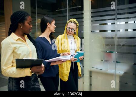 Drei schöne Geschäftsfrauen, die im Büro spazieren und über Projekt, Idee, Plan diskutieren. Nahansicht Foto. Kopierraum. Gespräch Stockfoto