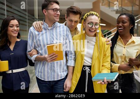 Start-up-Team freut sich über erfolgreichen Arbeitstag, positive junge Leute im stilvollen Kleidergespräch, lacht im Saal des modernen Bürogebäudes Stockfoto