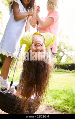 Gruppe Von Mädchen, Die Spaß Mit Freunden Haben, Die Auf Tire Swing In Garden Spielen Stockfoto