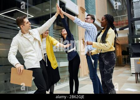 Motivierte junge fröhliche Leute, die Unterstützung zupften, die ihre Hände in eine Pyramide mit glücklichem begeistertem Ausdruck heben: Glück, Team, Freundschaft, r. Stockfoto