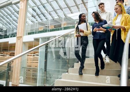 Junge ambitionierte, talentierte Büroangestellte sprechen, diskutieren ein neues Projekt, kopieren Raum, Studenten gehen im Gebäude, eine Gruppe junger Leute geht Stockfoto