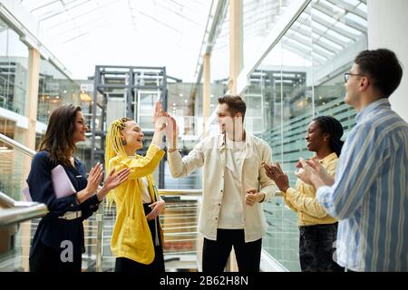 Junge Männer und Frauen feiern Erfolg. Stilvolle Frauen mit gelben Lachen und gutaussehende blonde Geschäftsleute geben hohe fünf. Nahaufnahme Stockfoto