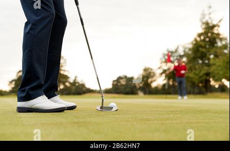 Nahaufnahme Des Weiblichen Golfspielers, Der Ball Auf Grün Setzt, Während Der Mann Flag Neigt Stockfoto