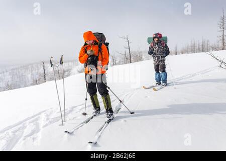 Blick auf die Höhe von zwei Skifahrern, die auf einem Bergrücken in den Ural-Bergen spazieren. Ein Wanderer, der in der Navigatorkarte sieht Stockfoto