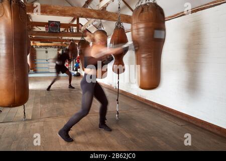 Action-Shot Von Boxern Für Männer Und Frauen Im Fitness-Studio Mit Ledertasche Stockfoto