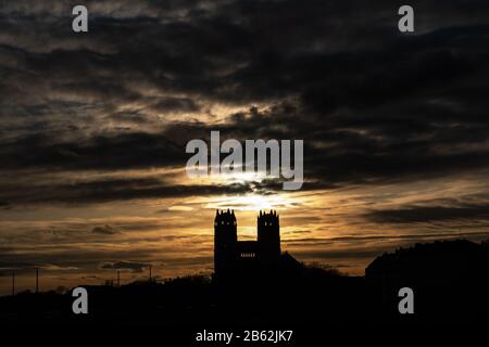 München, Deutschland. März 2020. Bei Sonnenuntergang verändern sich die Wolken am Himmel hinter den beiden Türmen der katholischen St.-Maximilian Kirche, die am Isarufer im Stadtteil Glockenbach steht. Kredit: Peter Kneffel / dpa / Alamy Live News Stockfoto