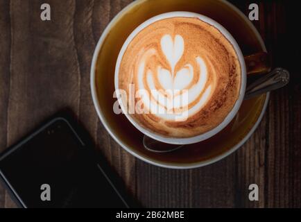 Top-down-Bild eines Latte- und Mobiltelefons, das die Kaffeekultur oder den Lebensstil von Millennials am Wochenende zeigt Stockfoto