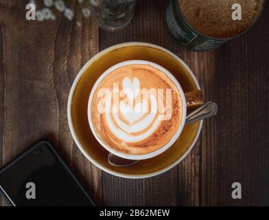 Top-down-Bild eines Latte- und Mobiltelefons, das die Kaffeekultur oder den Lebensstil von Millennials am Wochenende zeigt Stockfoto