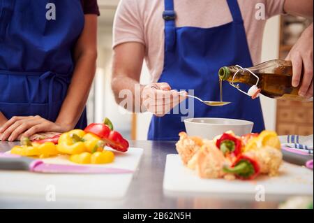 Erwachsene Männer Und Frauen, Die In Der Kochklasse Olivenöl Zum Gericht Hinzufügen Stockfoto