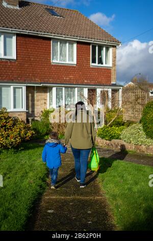 Eine Mutter und ein junger Sohn halten die Hände, die einen Gartenpfad zu einem Haus hinauf gehen Stockfoto