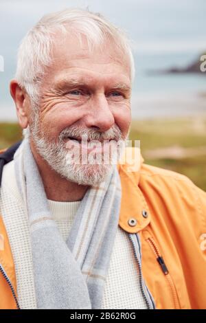 Active Senior Man Geht Im Herbst Oder Winter Auf Dem Küstenweg Durch Gate Mit Strand Und Klippen Dahinter Stockfoto