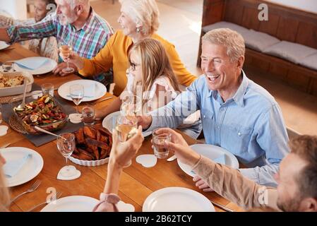 Familie der Multi-Generation, Die Einen Toast Mit Wein Macht, Während Sie Sich Zu Hause Zum Essen Treffen Stockfoto
