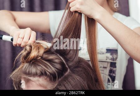 Haarstylisten mit einem Eisenkugeln eines weiblichen Klienten in einem Friseursalon, Nahansicht Stockfoto