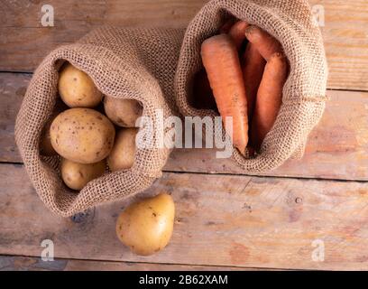 Kartoffeln und Karotten in einem Sacktuch auf einem Holztisch. Öko Concept Stockfoto