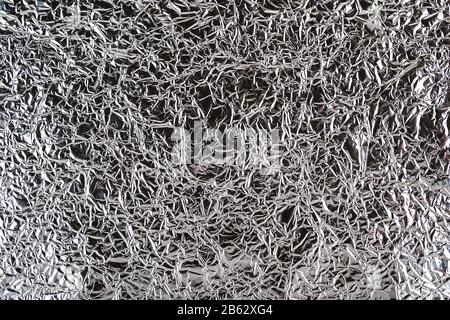 Geknitterte Aluminiumfolie. Blatt aus zerknitterter Silberfolie mit glänzenden Falten für den Hintergrund. Metallene zerknitterte Oberfläche als grafische Ressource. Draufsicht. Stockfoto