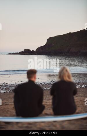 Entschärfte Aufnahme Eines Paares In Wetsuits Auf Surfstaycation Auf Surfbrett Mit Blick Auf See Stockfoto