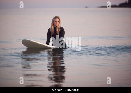 Frau Mit Wetsuit Sitzend Und Schwebend Auf Surfbrett Am Ruhigen Meer Stockfoto