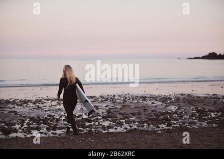 Frau, Die Surfbrett Mit Wetsuit Trägt, Während Sie Ins Meer Läuft Stockfoto