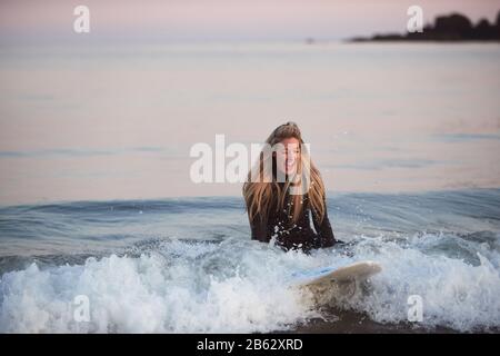 Frau, Die Auf Surfboard Riding Wave In Beach Sitzt Und Wetsuit Trägt Stockfoto