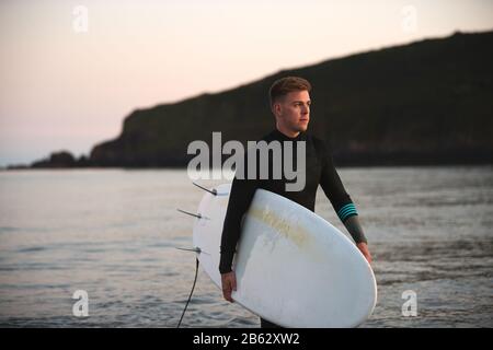 Mann, Der Einen Wetsuit Trägt, Der Surfboard Trägt, Während Er Aus Dem Meer Läuft