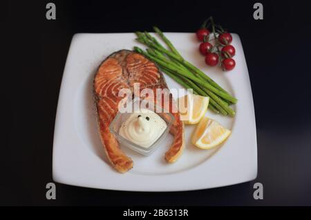 Lachssteaks mit Gemüse und Gewürzen: Spargel, Tomaten, Ingwer, Pfefferkörner, Salz, Chili, Zwiebel, Zitrone und Olivenöl auf schwarzem Grund. Heilen Stockfoto