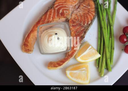 Lachssteaks mit Gemüse und Gewürzen: Spargel, Tomaten, Ingwer, Pfefferkörner, Salz, Chili, Zwiebel, Zitrone und Olivenöl auf schwarzem Grund. Heilen Stockfoto