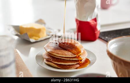 Ahorn-Sirup, Der Für Den Pancake-Tag Auf Den Stapel Frisch Zubereiteter Pfannkuchen Oder Crepes Auf Dem Tisch Gegossen Wird Stockfoto