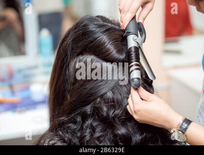 Stylist im friseursalon mit Eisenkügeln für brünette Haarkräuseln, Nahaufnahme Stockfoto