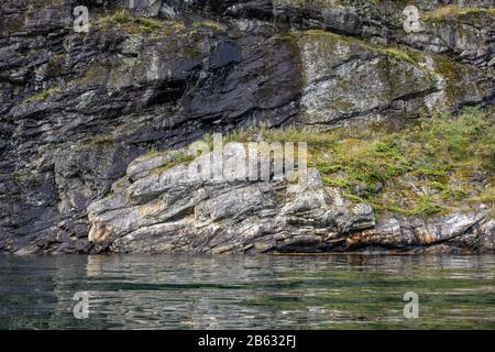 Schwere graue Felsen mit grünem Gras und Wasserspiegelung, norwegischer Fjord Aurlandsfjord. Helle Aussicht auf wilde Berge, Natur Norwegens. Kajak Scand Stockfoto