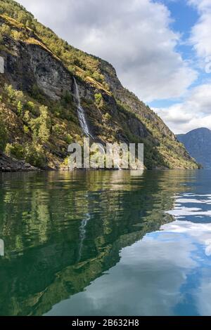 Wasserfall fällt, norwegischer Fjord Aurlandsfjord Spiegelreflexion. Helle vertikale Sicht auf wilde Berge in der Natur Norwegens. Sonniger Tag in Scandi Stockfoto