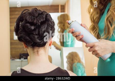 Schönheits-, Frisur- und Personen-Konzept - Nahaufnahme von Kopf- und Stylisten-Händen mit Haarfixspray zum Haarmachen im Salon Stockfoto