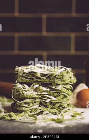 Italienische Nudelgerichte Hintergrund. Vegane italienische Pasta frisch mit Spinat (Spinat Fettuccine Alfredo Pasta) auf dunklem Hintergrund. Alter Küchenhintergrund. Stockfoto