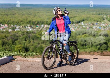 Sport junge Frau trinkt Wasser, nachdem sie eine Fahrradübung gemacht hat Stockfoto