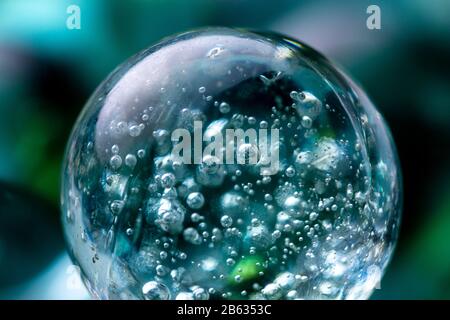 Makroaufnahmen von Luftblasen in einer Glaskugel aus Marmor, die in dem durchsichtigen blau gefärbten, glatten Stein aus blauem Teelicht reflektiert werden. Stockfoto