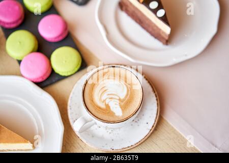 Frühstück im Café, Morgenkaffee. Cappuccino und viele Desserts auf dem Tisch. Napoleon, Schokoladenkuchen, Käsekuchen und Makronen. Stockfoto