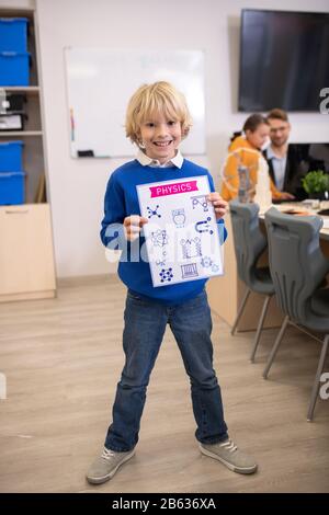 Blonder Junge steht und hält Papier mit Physik-Zeichnungen Stockfoto