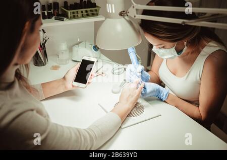 Frau in ein Nagelstudio, Maniküre, durch eine Kosmetikerin. In den Händen von Client-Smartphone Stockfoto