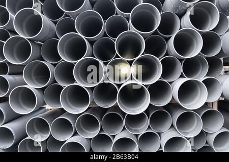 Graue PVC-Rohre, Kunststoffrohre, die in Reihen gestapelt sind und durch die eine Lichtausdünnung erfolgt Stockfoto