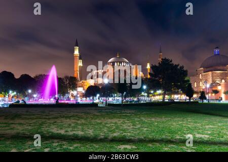 Die Hagia Sophia-Moschee und das Museum mit dem bunten Wasserbrunnen und dem Park, der am Abend auf dem Sultanahmet-Platz in Istanbul, Türkei, beleuchtet wird. Stockfoto