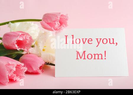 "Ich liebe dich, Mama"-Text auf Geschenkkarte in Blumenstrauß auf pinkfarbenem Hintergrund. Grußkarte für Mama. Tag Der Glücklichen Mütter. Blumenlieferung. Glückwunschkarte Stockfoto