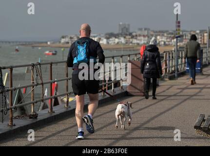 Shoeburyness. Großbritannien. Februar 2020. Ein Mann nimmt seinen Hund zum Joggen entlang der Promenade mit einem Rucksack. Southend on Sea ist im Hintergrund zu sehen. Entlang des Strandes bei Shoeburyness. Essex. GROSSBRITANNIEN. 19/02/2020. Credit Garry Bowden/Sport in Pictures/Alamy Stockfoto